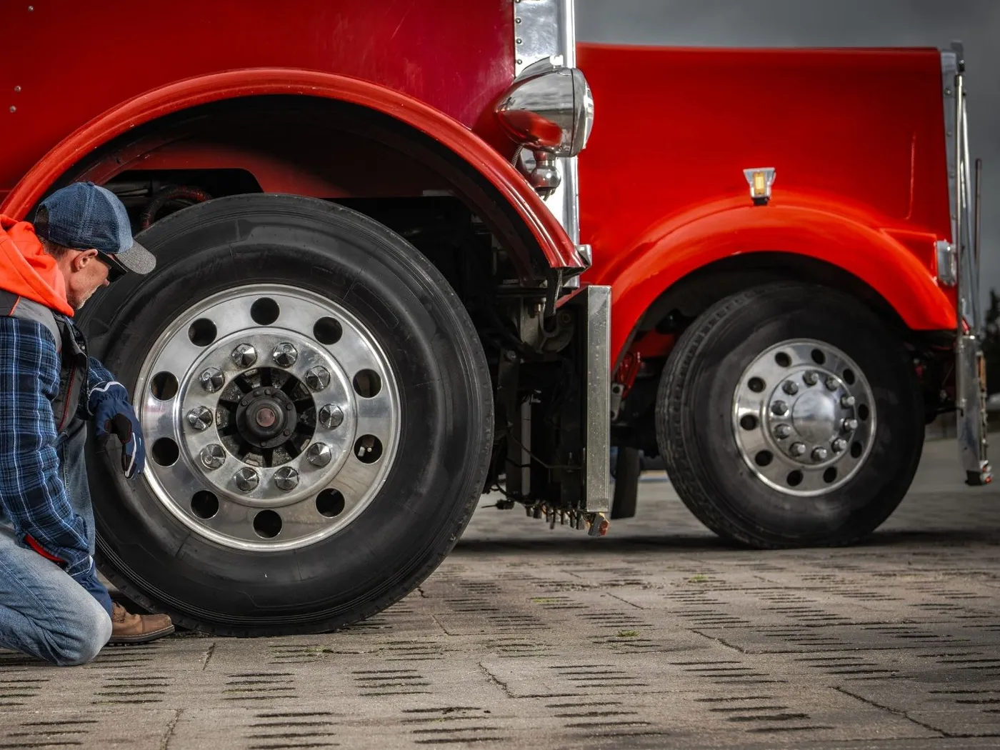 Mechanic kneeling to service the wheel end of a red semi truck
