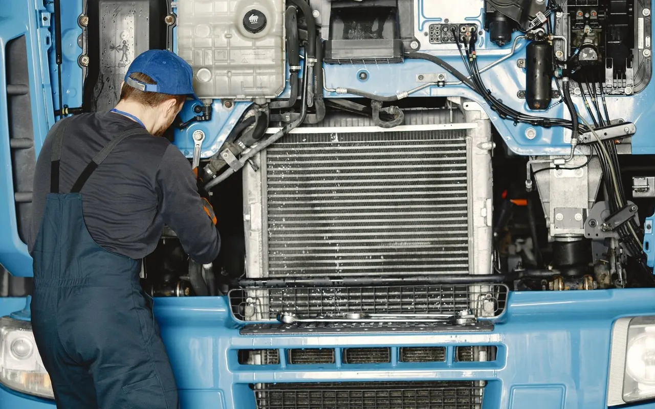 Technician working on the open front end of a blue heavy truck
