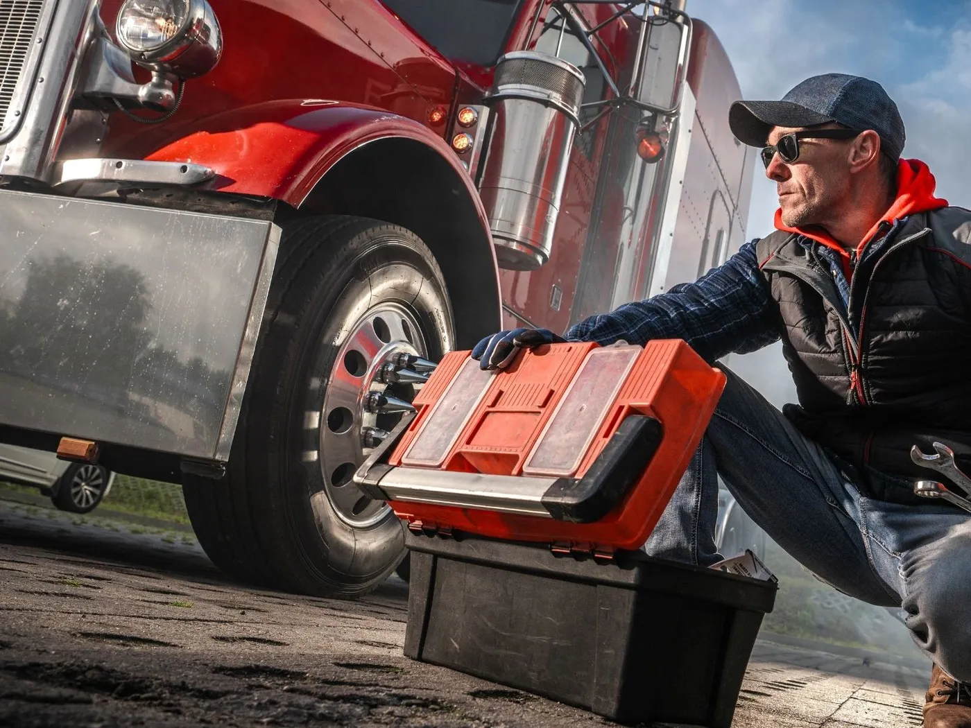 Mobile mechanic kneeling beside a semi truck wheel with an open tool case